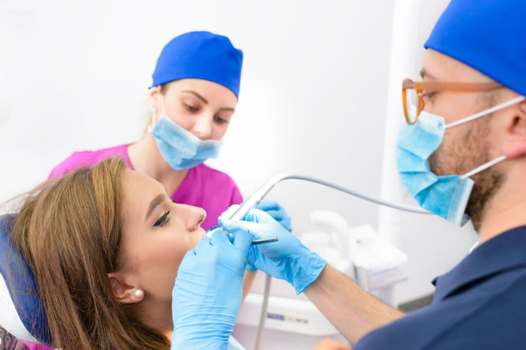 A dentist and dental assistant perform a routine oral examination on a patient using professional dental instruments in a modern dental clinic. The image represents preventive dental care, comprehensive dental exams, and teamwork during patient treatment.