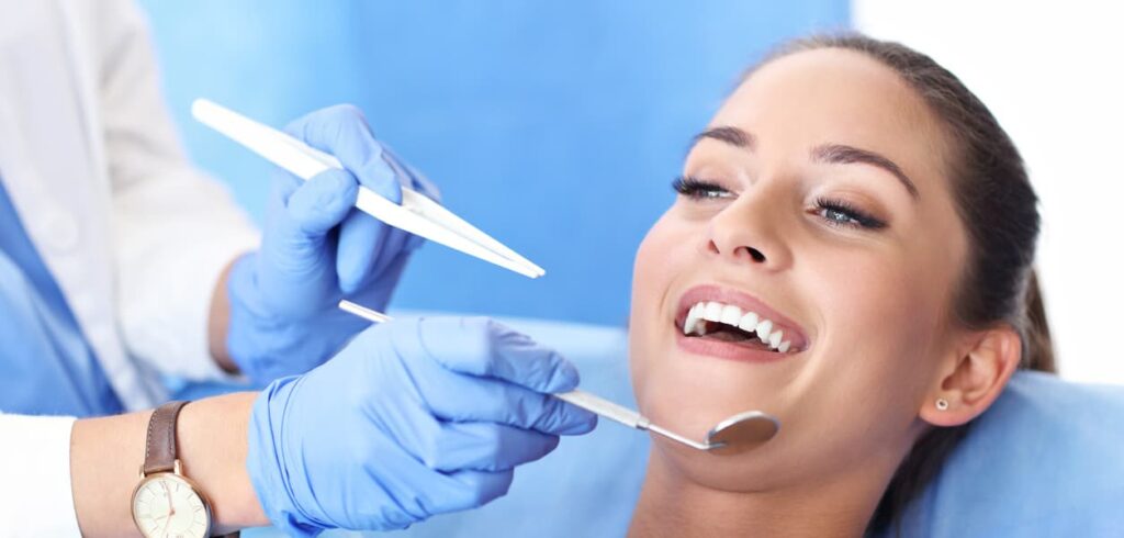 A smiling patient reclines in a dental chair while a dentist performs a routine oral examination using a dental mirror. The image highlights preventive dental care, regular checkups, and a comfortable patient experience in a modern dental clinic.