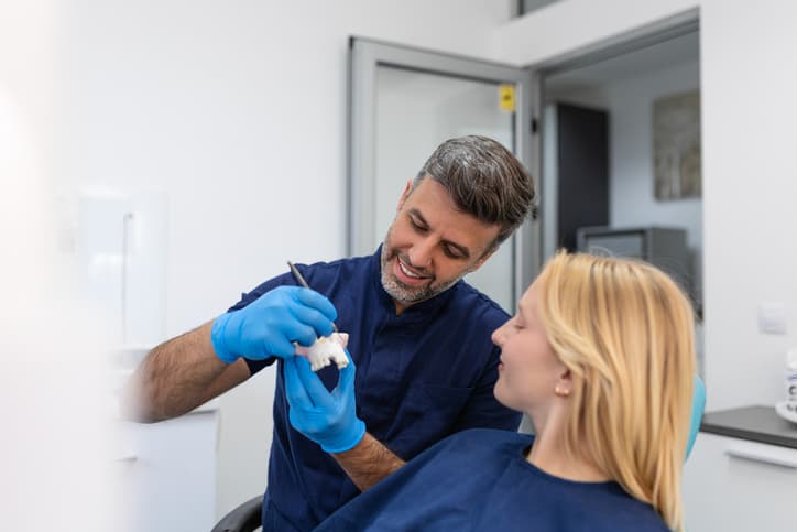 Dentist showing a dental model to a patient while explaining treatment options during a consultation in a modern dental clinic.