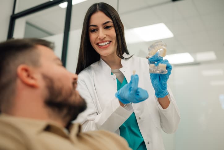 Dental professional showing a patient a tooth model and dental restoration while discussing options for dental crowns and bridges.