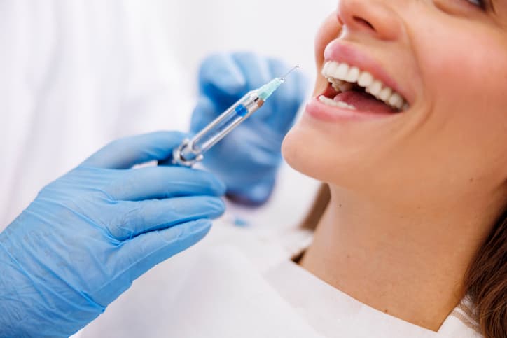 Cosmetic injectable treatment being prepared near a smiling woman’s mouth